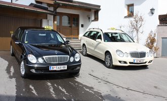 Two taxis are standing in front of a building. The black taxi is a limousine and the white taxi is an estate car. | © Taxi Beranek | Elmar Beranek