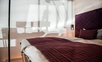 Ein modernes Schlafzimmer mit einem großen Bett und einer eleganten Bettdecke. Die sanften Schatten von Fenstern und Möbeln verleihen dem Raum eine entspannte Atmosphäre. | © Türtscher Die Schreinermanufaktur