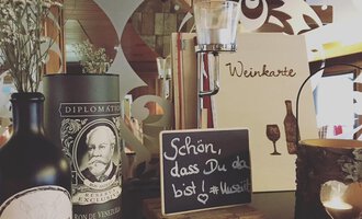 An inviting restaurant scene with wine lists, decorative bottles, and a small sign that reads "Nice to have you here!". In the background, stylish wooden elements and candles are visible. | © Uusziit | Chantal Kessler