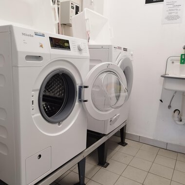 A laundry room with several washing machines on a tiled floor. In the background, there is a sink. | © Kleinwalsertal Tourismus | N. Lughammer