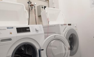 A washing machine and a dryer stand next to each other in a small laundry room. The appliances are modern and in good condition. | © Kleinwalsertal Tourismus | N. Lughammer