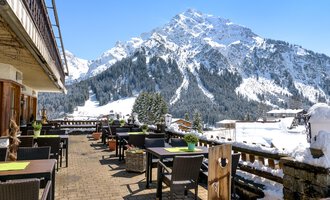 A terrace with tables and chairs, surrounded by snow-covered mountains. The clear blue sky gives the landscape a picturesque atmosphere. | © Wirtshaus Hoheneck | Klaus Ruland