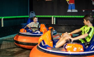 Two children are riding electronic bumper cars in a sports hall. One of the children has an expression full of joy and excitement on their face. | © Wonniland Sonthofen | interSPA Gruppe
