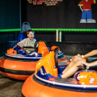 Two children are riding electronic bumper cars in a sports hall. One of the children has an expression full of joy and excitement on their face. | © Wonniland Sonthofen | interSPA Gruppe