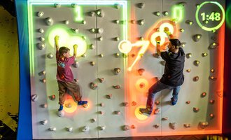 Two children are climbing on an interactive climbing wall with colorful lights. The time is running out and there are various colored holds. | © Wonniland Sonthofen | interSPA Gruppe