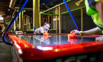A child is happily playing at an air hockey table. The room is brightly colored and invitingly designed. | © Wonniland Sonthofen | interSPA Gruppe