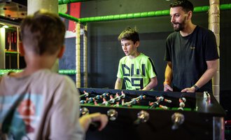 Two boys are playing table football while an adult watches. The atmosphere is lively and friendly. | © Wonniland Sonthofen | interSPA Gruppe