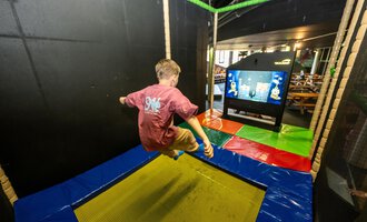 A boy is jumping on a trampoline in a play area. In the background, a screen displaying game content can be seen. | © Wonniland Sonthofen | interSPA Gruppe