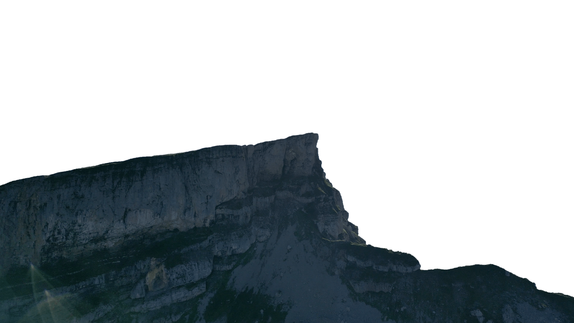 Silhouette of a rugged mountain ridge against a bright white sky.